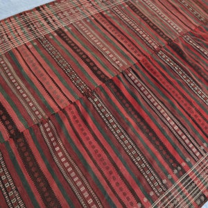 May include: A red, green, and black striped rug with a geometric pattern. The rug is woven with a variety of textures and colors.