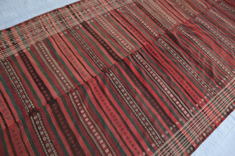 May include: A red, green, and black striped rug with a geometric pattern. The rug is woven with a variety of textures and colors.