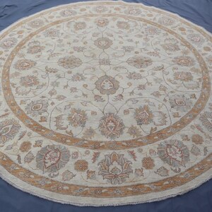 May include: A large round area rug featuring an intricate floral pattern in shades of cream, beige, and muted orange. The design includes symmetrical botanical motifs and scrolling vines arranged in a circular composition with a wide decorative border.
