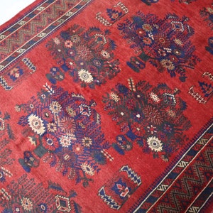 May include: A red rug with a traditional Persian design featuring blue and cream floral motifs. The rug has a geometric border with a dark blue and cream pattern.