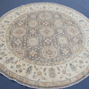 May include: A round area rug with a central medallion design in shades of gray, beige, and brown. The rug features a detailed border with floral and geometric patterns. The rug's diameter is approximately 6 feet.