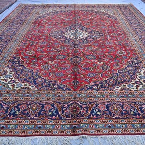 May include: A large, rectangular red rug with an intricate floral pattern and a navy blue border. The rug features a central medallion design and detailed corner motifs. The edges have a fringe.