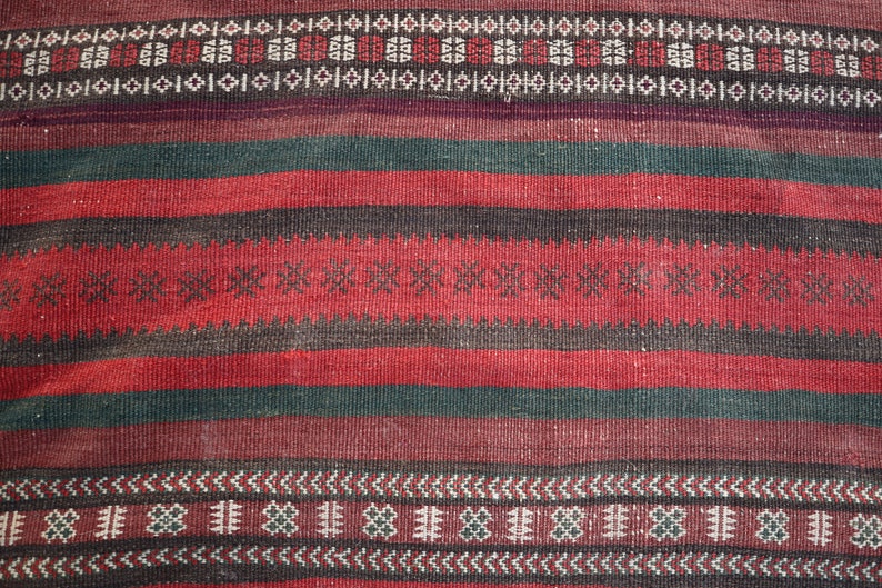 May include: A close-up of a red, black, and green woven rug with intricate geometric patterns. The rug has a traditional design and is made of natural fibers.