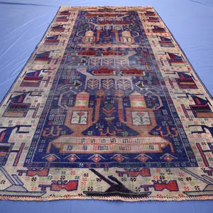 May include: A rectangular area rug featuring a deep blue central field with intricate geometric patterns, stylised animal figures, and floral motifs. The border displays a repeating sequence of dark blue and red shapes on a light beige background.