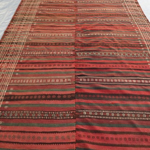May include: A red, green, and black striped rug with intricate woven patterns. The rug has a fringed edge and is made of natural fibers.