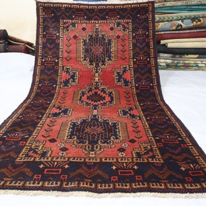 Könnte beinhalten: Ein traditioneller persischer Teppich mit einem geometrischen Muster in Rot, Blau und Gold. Der Teppich hat einen Fransenrand und ist aus Wolle gefertigt.