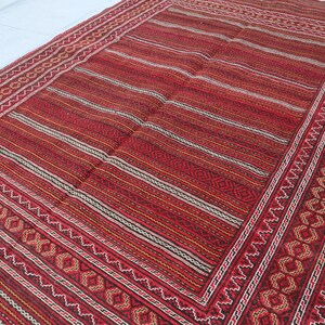 Puede incluir: Una alfombra roja, negra y blanca a rayas con un borde de patr&oacute;n geom&eacute;trico. La alfombra tiene un aspecto y una sensaci&oacute;n de tejido tradicional.