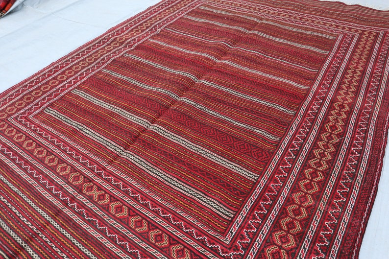 Puede incluir: Una alfombra roja, negra y blanca a rayas con un borde de patr&oacute;n geom&eacute;trico. La alfombra tiene un aspecto y una sensaci&oacute;n de tejido tradicional.