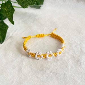 Könnte beinhalten: Ein geflochtenes Armband in Gelb und Weiß mit einem Gänseblümchenmuster.