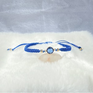 May include: A blue braided bracelet with a gold accent and a blue gemstone in the centre.