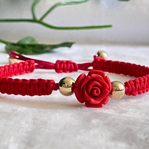 Puede incluir: Pulsera de cuerda roja con un dije de rosa roja y cuentas doradas.