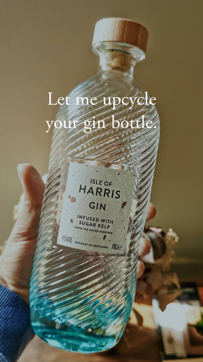 May include: A clear glass bottle of Isle of Harris Gin, infused with sugar kelp from the Outer Hebrides. The bottle has a blue and white swirl design and a wooden top.