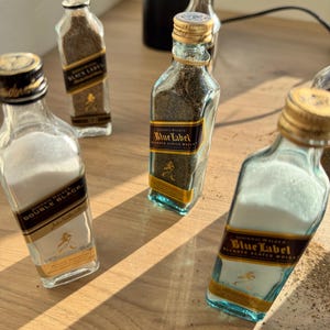May include: Five miniature glass bottles filled with spices. The bottles are labeled with the Johnnie Walker logo and the text "Black Label", "Double Black", and "Blue Label".