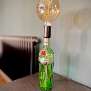 May include: A green glass bottle with a black cap and a clear light bulb on top. The bottle has the text "Tanqueray No. TEN" on the label.