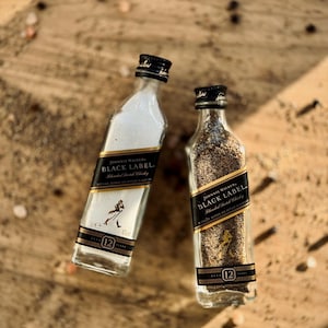 May include: Two miniature glass bottles filled with salt and pepper. Both bottles are labeled with the Johnnie Walker Black Label logo and the text "Blended Scotch Whisky".