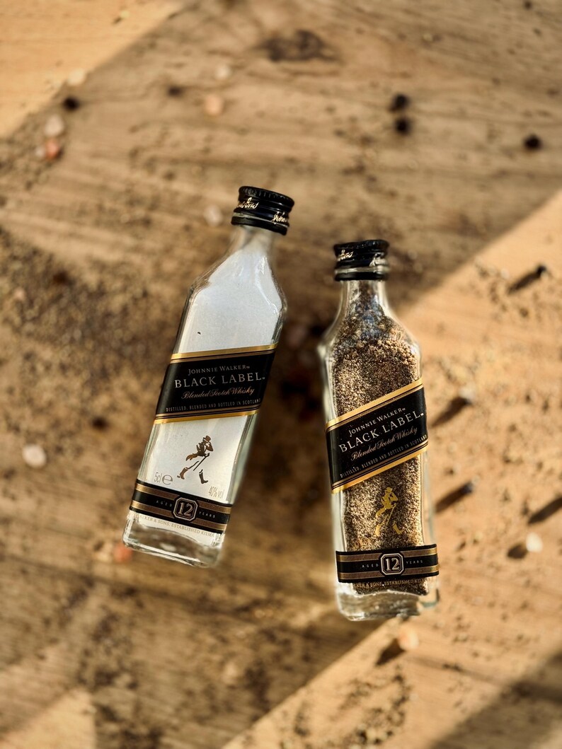 May include: Two miniature glass bottles filled with salt and pepper. Both bottles are labeled with the Johnnie Walker Black Label logo and the text "Blended Scotch Whisky".