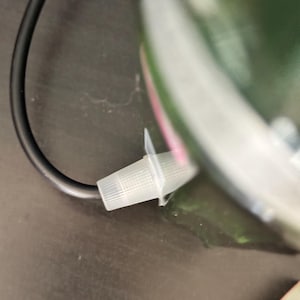 May include: A close-up of a black electrical cord with a white plastic connector. The connector is attached to a green object.