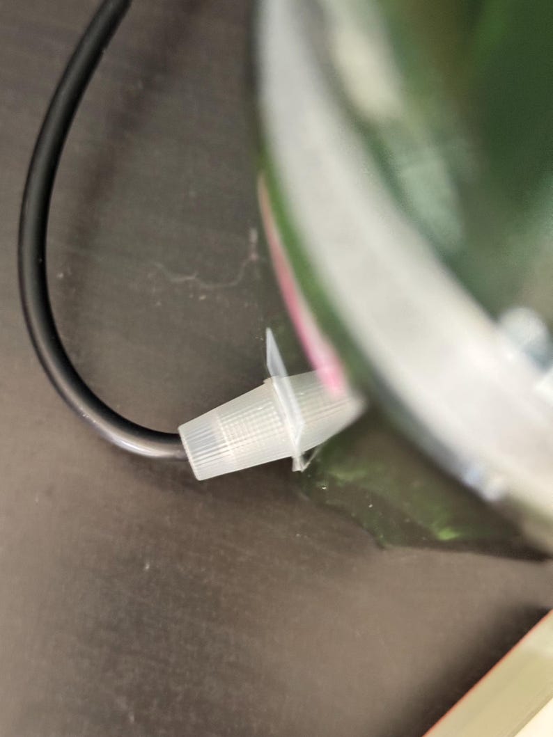 May include: A close-up of a black electrical cord with a white plastic connector. The connector is attached to a green object.