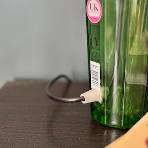May include: A green glass bottle with a black cord and a white plug attached to the bottom. The bottle has a label with the text "UK" on it.