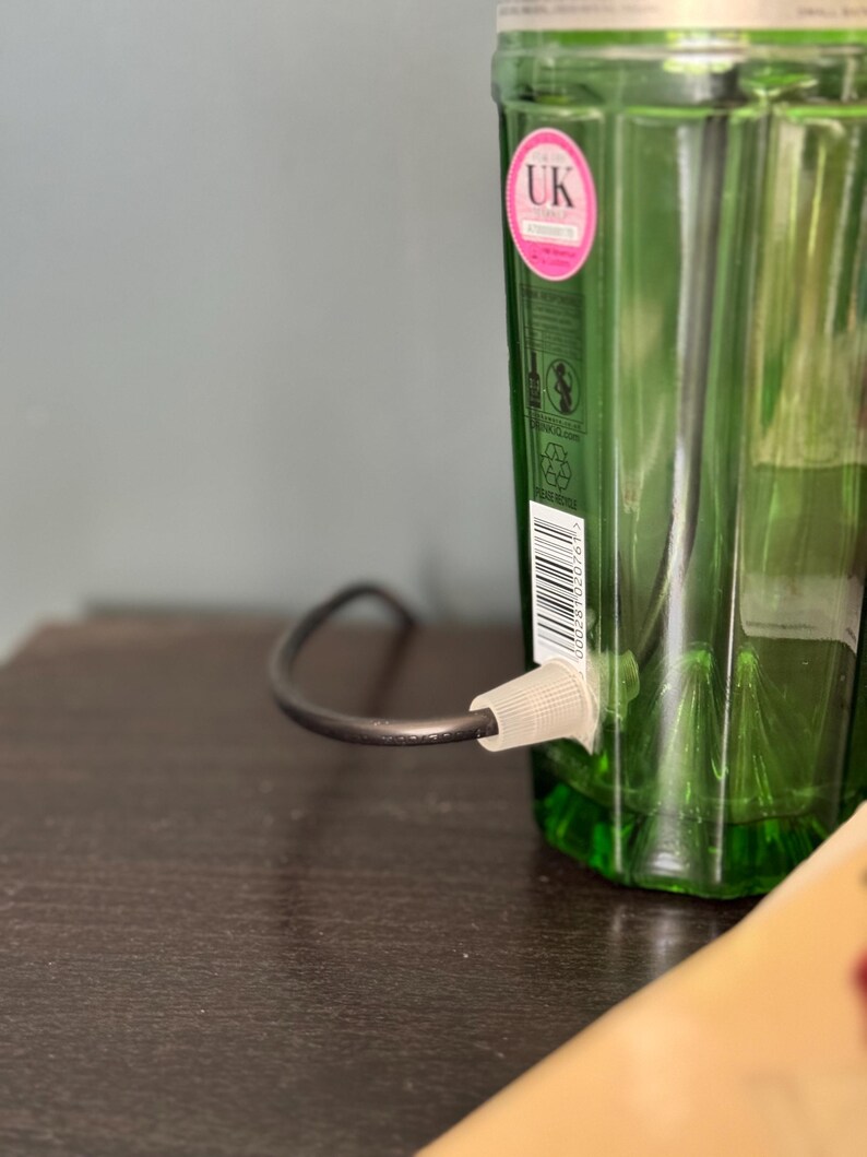 May include: A green glass bottle with a black cord and a white plug attached to the bottom. The bottle has a label with the text "UK" on it.