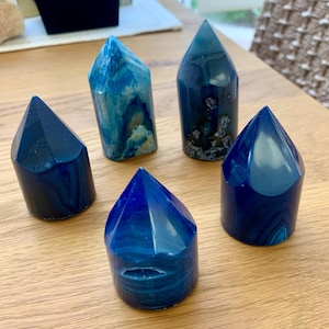 Peut inclure: Cinq pointes de cristal d'agate bleue, chacune avec un motif unique de bandes bleues et blanches. Les pointes sont disposées en cercle sur une surface en bois.