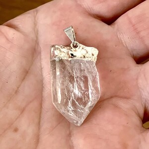 Quartz brut naturel en pendentif vu dans la main  EN : Raw natural quartz crystal pendant shown in hand