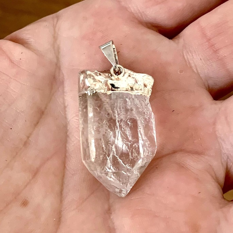 Quartz brut naturel en pendentif vu dans la main  EN : Raw natural quartz crystal pendant shown in hand