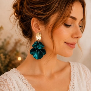 May include: Gold-tone and teal green petal earrings. The earrings feature a rectangular gold stud and three overlapping teal green petal shapes. The earrings are a bold statement piece, perfect for adding a touch of elegance to any outfit.