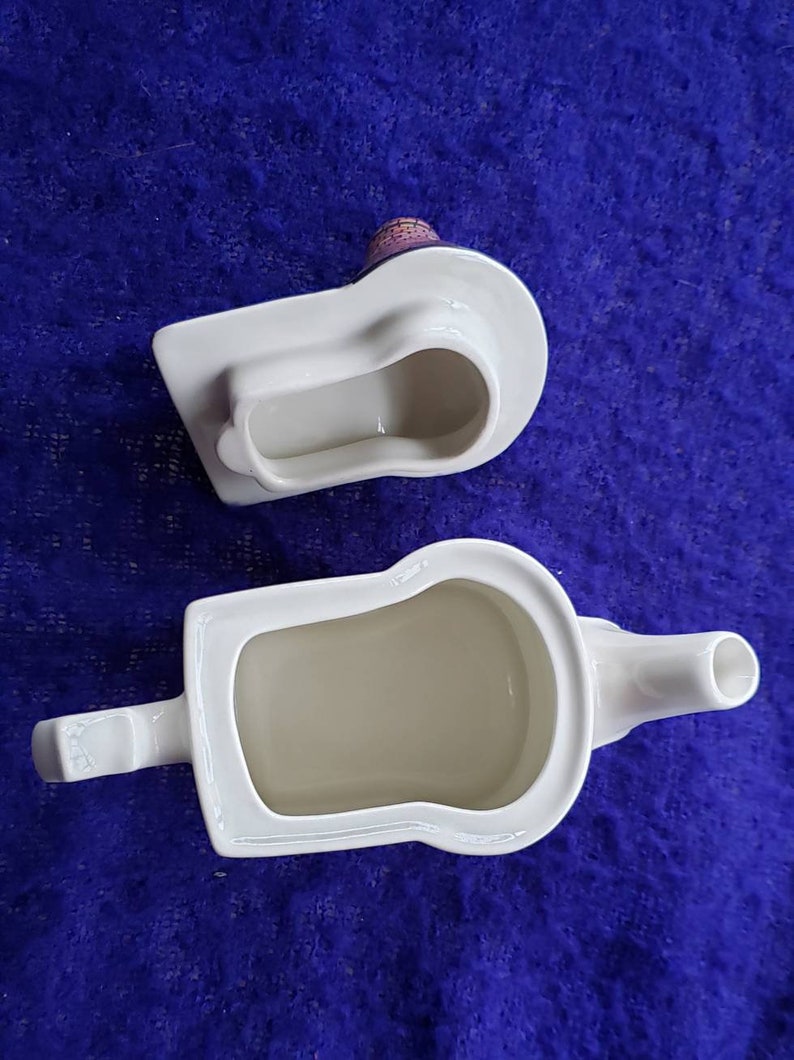 May include: White ceramic teapot with a spout and handle, shaped like a loaf of bread. The teapot is empty and the inside is visible. The lid is separate and is also shaped like a loaf of bread.