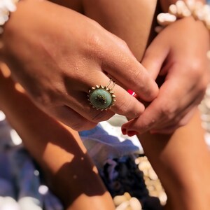 Peut inclure: Une bague en or avec une pierre verte et un motif décoratif. La bague est sur le doigt d'une personne.