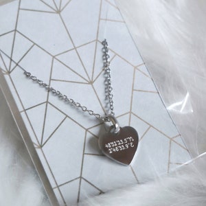 Può includere: Una collana d'argento con un ciondolo a forma di cuore. Il ciondolo ha le coordinate "48.52'23.5"N 2'46'33.9"E" incise su di esso.
