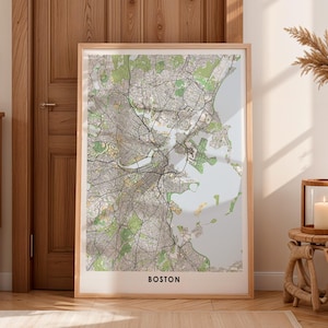Puede incluir: Impresión enmarcada del mapa de Boston, Massachusetts, con diseños detallados de calles y parques en tonos grises, verdes y beige. El nombre de la ciudad está impreso en una fuente en negrita, sin serifa, en la parte inferior. El mapa está encerrado en un marco de madera clara.