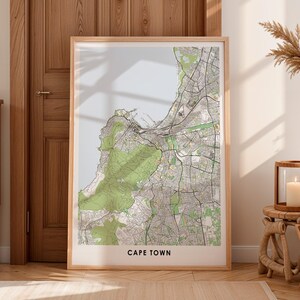 Puede incluir: Una impresión enmarcada de un mapa de Ciudad del Cabo, Sudáfrica, en una paleta de colores neutros. El mapa presenta diseños de calles detallados, áreas verdes y el texto "CAPE TOWN" en la parte inferior. El marco es de color madera clara.