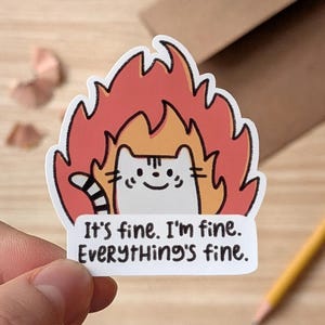 May include: A white cat sticker with a striped tail, surrounded by orange and red flames. The sticker has the text "It's fine. I'm fine. Everything's fine." on a white rectangle.