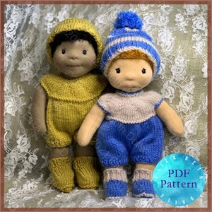 May include: Two handmade cloth dolls. One doll wears a yellow knitted romper and matching hat and booties. The other doll wears a blue and white striped hat, a blue romper, and a beige and blue knitted top and booties. The dolls are standing side by side.