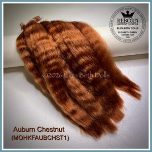 May include: A bundle of wavy auburn chestnut hair fibers for doll making. The image includes a circular Reborn Artistry Alliance logo, the text 2026 Eliza Beth Dolls, and the label Auburn Chestnut (MOHKFAUBCHST1) printed in brown text.