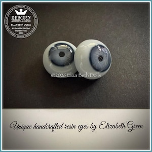 May include: Two handcrafted resin doll eyes with a blue iris and a black pupil. The eyes are white with a glossy finish. The image text reads "Unique handcrafted resin eyes by Elizabeth Green."