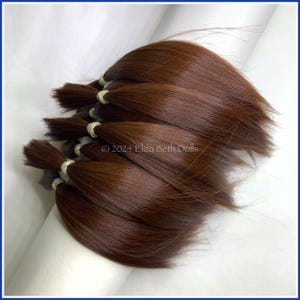 May include: Multiple strands of brown human hair extensions, tied together with elastic bands. The hair is smooth and silky, and appears to be of high quality.