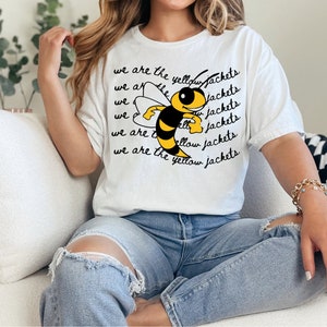 Op de afbeelding: Wit T-shirt met een cartoon-bij en de tekst "We are the yellow jackets" die meerdere keren wordt herhaald.
