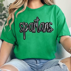 Może przedstawiać: Zielona koszulka z napisem "spartans" w srebrnych literach z brokatu.