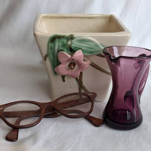 Peut inclure: Un pot en céramique blanche avec un motif floral représentant une fleur rose et des feuilles vertes. Un pichet en verre violet et des lunettes brunes sont également présents sur l'image.