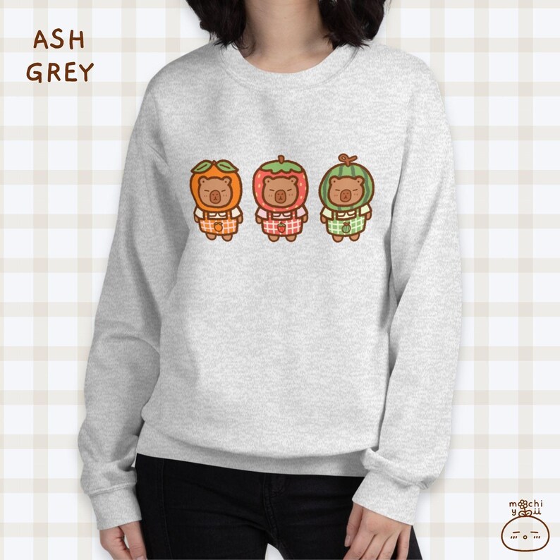 K&ouml;nnte beinhalten: Ein graues Sweatshirt mit einem Aufdruck von drei braunen B&auml;ren, die Fruchtkost&uuml;me tragen. Die B&auml;ren tragen ein orangefarbenes, rotes und gr&uuml;nes Fruchtkost&uuml;m. Das Sweatshirt hat einen Rundhalsausschnitt und lange &Auml;rmel.