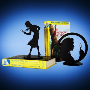 May include: Black metal detective-themed bookends with a silhouette of a woman holding a magnifying glass. Two yellow Nancy Drew books are visible, along with a book titled "The Secret of the Old Clock". The bookends add a decorative touch to any bookshelf.