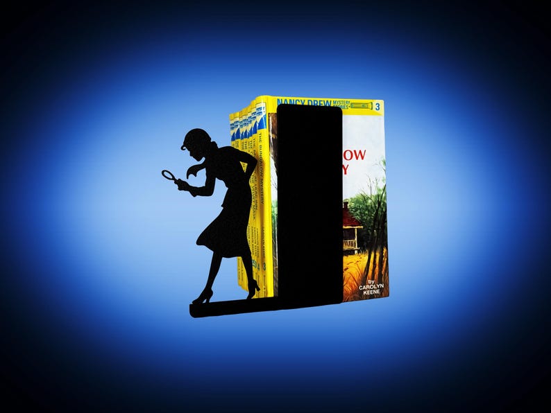 May include: A black metal bookend featuring a silhouette of a woman holding a magnifying glass, positioned as if investigating. The bookend is placed between a stack of yellow and white books, with the title "Nancy Drew" visible.