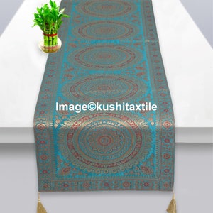 May include: A teal blue table runner with gold and red embroidered circular patterns. The runner has tassels on each end.
