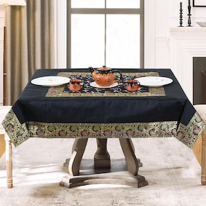 May include: Black square tablecloth with a gold and floral border. The tablecloth is set on a wooden table with a teapot and cups.