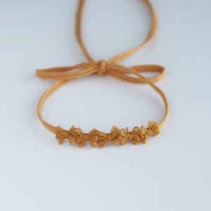 May include: A mustard yellow headband with a row of small fabric bows.