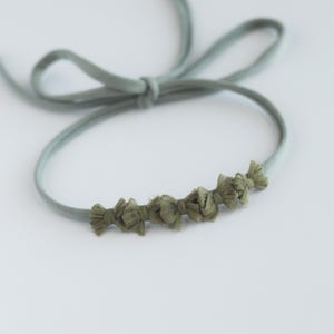 May include: A light green headband with a row of small green fabric bows.