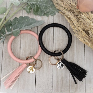 May include: Two leather keychains with gold rings and tassels. One keychain is black with a white monogram "CDR" and the other is pink with a white monogram "A".