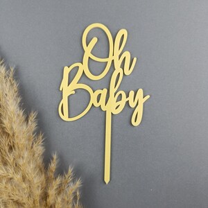 May include: A wooden cake topper with the words "Oh Baby" in a cursive font. The topper is a light brown color and is perfect for a baby shower or gender reveal party.
